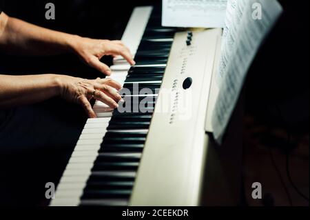 Vista laterale delle mani di crop del musicista seduto e suonando pianoforte elettrico. Foto Stock