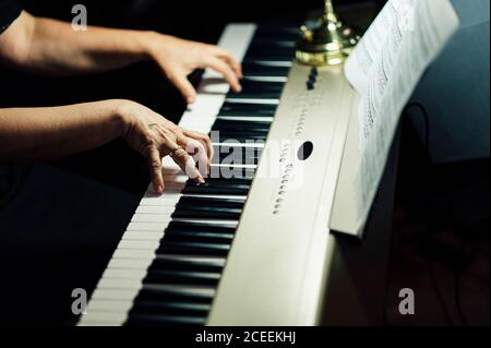 Vista laterale delle mani di crop del musicista seduto e suonando pianoforte elettrico. Foto Stock