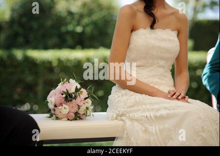 Crop felice coppia newlywed seduta su panchina nel giardino e tenendo le mani. Foto Stock