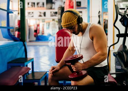 uomo in cuffia che ascolta musica e che si esercita con il manubrio in palestra. Foto Stock