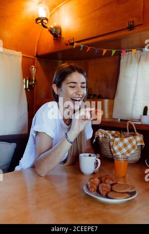 Bella giovane donna che tiene un piccolo mordicchietto e ridere mentre fa colazione in un furgone accogliente Foto Stock