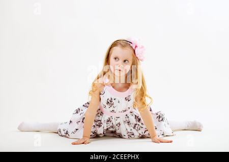 Bambina bionda in un vestito seduto sullo spago davanti allo sfondo bianco Foto Stock