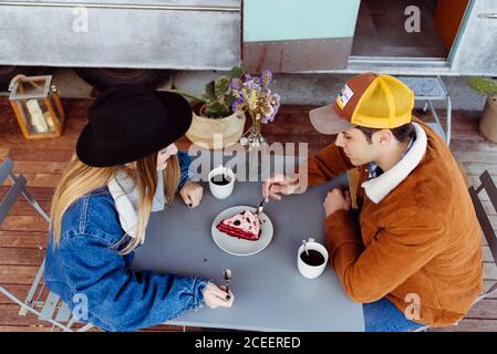 Giovane uomo e donna gustando una deliziosa torta mentre si siede al tavolo vicino a un pulmino grungy Foto Stock