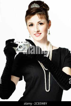 Ritratto di una bella giovane ed elegante donna con una fotocamera d'epoca isolata su sfondo bianco. La ragazza nell'immagine di Audrey Hepburn Foto Stock