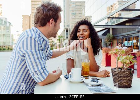 Bella afro-americana donna e bel caucasico uomo sorridendo e guardando l'un l'altro mentre si passa il tempo in caffè all'aperto insieme Foto Stock