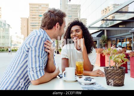 Bella afro-americana donna e bel caucasico uomo sorridendo e guardando l'un l'altro mentre si passa il tempo in caffè all'aperto insieme Foto Stock