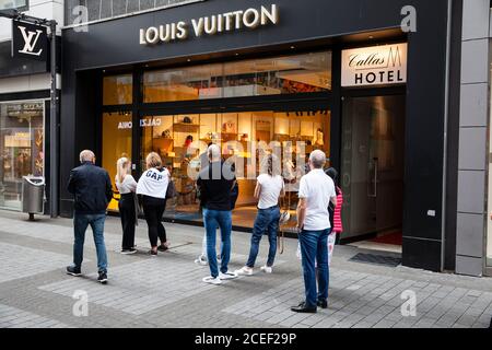 Per rispettare le norme sulla distanza durante la pandemia di Corona, i clienti stanno aspettando di fronte al negozio Louis Vuitton sulla via dello shopping Hohe St Foto Stock