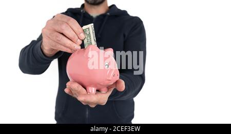 sezione centrale dell'uomo che tiene la banca del piggy in una mano e. inserire la bolletta del dollaro in essa con l'altro Foto Stock