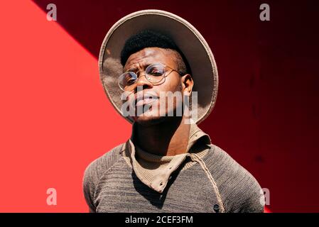 Giovane africano maschio in maglione cappello bianco e occhiali sopra sfondo rosso Foto Stock