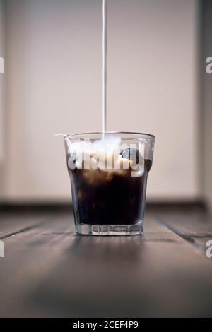 Versare il latte sul caffè ghiacciato scuro nel bicchiere posto su tavolo di legno Foto Stock