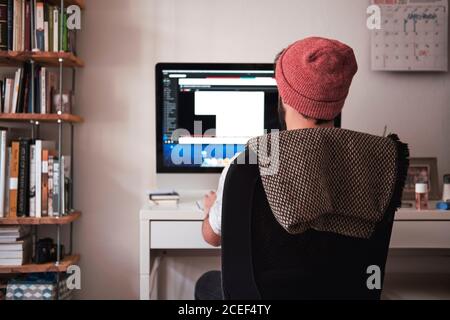 Vista posteriore dell'uomo freelance seduto sul posto di lavoro e in uso Computer di cancelleria a Monaco Foto Stock