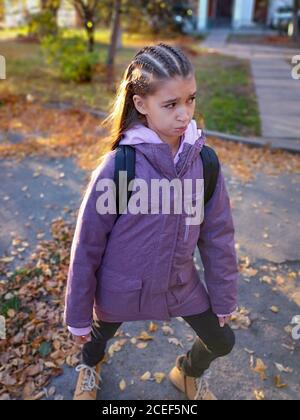 Bambina giovane con cornbraids e in abiti casual che fanno il bouda su sfondo autmn. Foto Stock