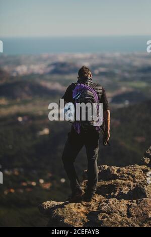 Vista posteriore dell'uomo con zaino e attrezzatura da arrampicata in piedi Sulla cima del monte Garbi e guardando la natura maestosa Il giorno di sole a Gibuti Foto Stock