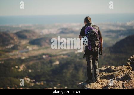 Vista posteriore dell'uomo con zaino e attrezzatura da arrampicata in piedi Sulla cima del monte Garbi e guardando la natura maestosa Il giorno di sole a Gibuti Foto Stock