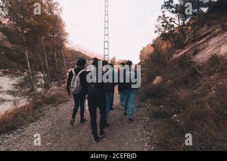 Vista posteriore del gruppo di persone con zaini che camminano lungo percorso nella campagna autunnale insieme Foto Stock