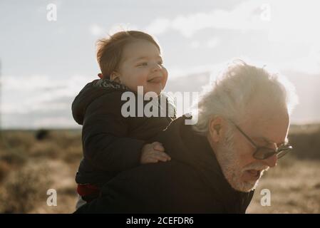 Uomo anziano che porta il nipote sulla schiena Foto Stock