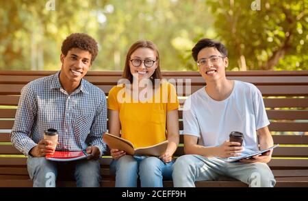 Tre studenti seduti sul banco relax con caffè all'aperto Foto Stock