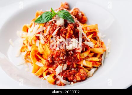Vista ravvicinata di una piastra in ceramica bianca piena di gustosi piatti italiani pasta con salsa di carne e formaggio grattugiato con potherb sopra in alto Foto Stock