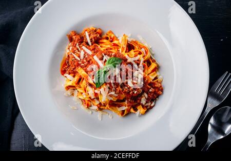 Vista ravvicinata di una piastra in ceramica bianca piena di gustosi piatti italiani pasta con salsa di carne e formaggio grattugiato con potherb sopra in alto Foto Stock