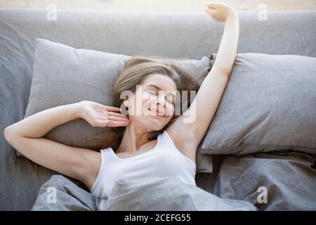 Bella giovane donna che si stretona su un comodo letto, essendo pigro la Domenica mattina, vista dall'alto Foto Stock