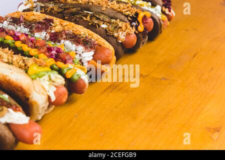 Fila di hot dog assortiti con diversi condimenti e ripieni deliziosi su tavola di legno. Foto Stock