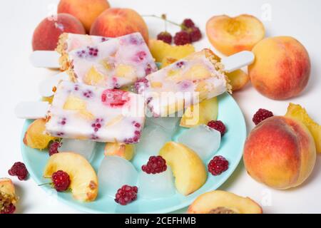 gelato estivo fresco su bastone con frutti di pesca e lamponi su sfondo chiaro. Foto Stock
