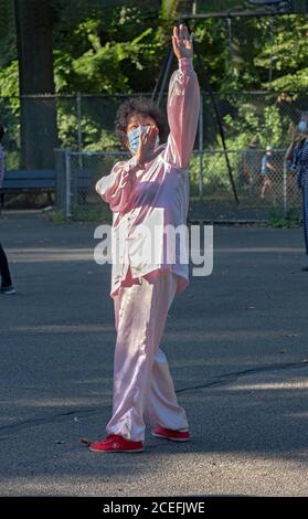 Una donna cinese più anziana americana che indossa un abito tradizionale tang, scarpe rosse e maschera chirurgica ad una lezione di Tai Chi in un parco a Flushing, Queens, New York. Foto Stock