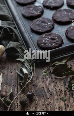 Secchezza ramo di oliva che giace vicino teglia da forno con set di biscotti al cioccolato senza glutine yummy su tavolo in legno di shabby Foto Stock