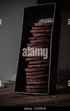 Contenitore in metallo con pila di biscotti al cioccolato senza glutine di yummy in piedi su vecchio tavolo di legno Foto Stock