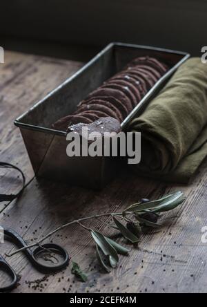 Piccolo rametto di olive asciutte adagiato su un piano di legno vicino al metallo scatola con deliziosi biscotti al cioccolato senza glutine e morbido asciugamano Foto Stock