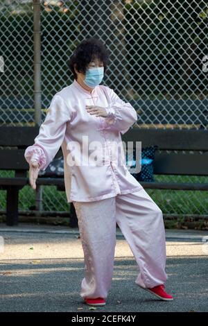 Una donna cinese più anziana americana che indossa un abito tradizionale tang, scarpe rosse e maschera chirurgica ad una lezione di Tai Chi in un parco a Flushing, Queens, New York. Foto Stock