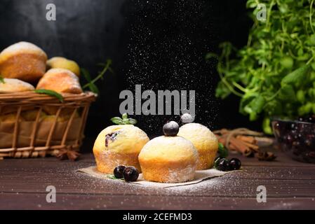 cupcake con foglie di menta e ribes nero in zucchero a velo su fondo nero, cesto di legno con cupcake e ribes nero. levitazione del po Foto Stock