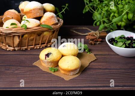 cupcakes con foglie di menta e ribes nero in zucchero in polvere su fondo nero, un cesto di legno con cupcakes e ribes nero . primo piano, spazio Foto Stock