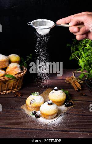 cupcake con foglie di menta e ribes nero in zucchero a velo su fondo nero, cesto di legno con cupcake e ribes nero. levitazione del po Foto Stock