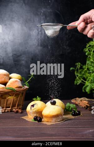 cupcake con foglie di menta e ribes nero in zucchero a velo su fondo nero, cesto di legno con cupcake e ribes nero. levitazione del po Foto Stock