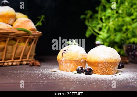 cupcakes con foglie di menta e ribes nero in zucchero in polvere su fondo nero, un cesto di legno con cupcakes e ribes nero . primo piano, spazio Foto Stock