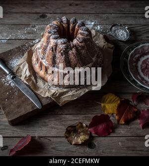 Fresco gustoso Kugelhopf in piedi su carta pergamena su legname stagionato piano portapaziente in prossimità di foglie autunnali asciutte Foto Stock