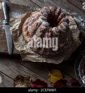 Fresco gustoso Kugelhopf in piedi su carta pergamena su legname stagionato piano portapaziente in prossimità di foglie autunnali asciutte Foto Stock