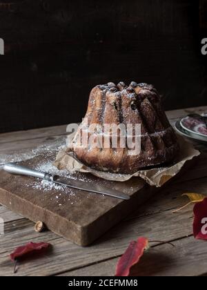 Fresco gustoso Kugelhopf in piedi su carta pergamena su legname stagionato piano portapaziente in prossimità di foglie autunnali asciutte Foto Stock
