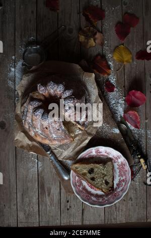 Delicate foglie autunnali giacciono su un tavolo in legno di scabvicino alla piastra E carta pergamena con yummy fresco Kugelhopf Foto Stock