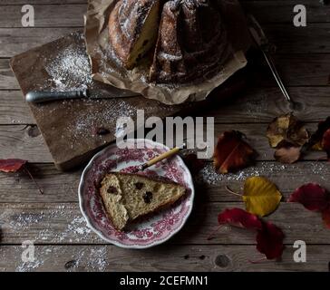 Delicate foglie autunnali giacciono su un tavolo in legno di scabvicino alla piastra E carta pergamena con yummy fresco Kugelhopf Foto Stock