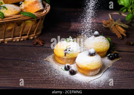 cupcake con foglie di menta e ribes nero in zucchero a velo su fondo nero, cesto di legno con cupcake e ribes nero. levitazione del po Foto Stock