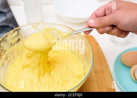 l'impasto per i cupcakes fatto di farina di riso, burro, uova, zucchero scorre dal cucchiaio. primo piano della consistenza dell'impasto in un piatto trasparente. Foto Stock