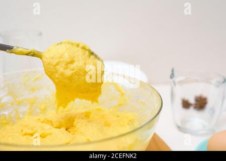 l'impasto per i cupcakes fatto di farina di riso, burro, uova, zucchero scorre dal cucchiaio. primo piano della consistenza dell'impasto in un piatto trasparente. Foto Stock