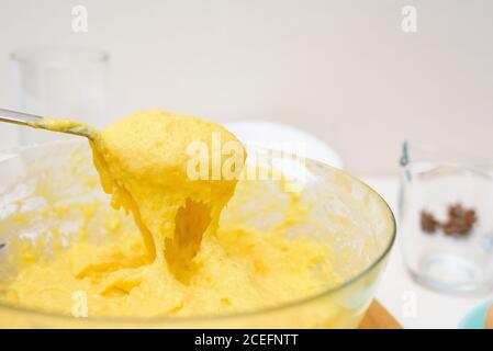 l'impasto per i cupcakes fatto di farina di riso, burro, uova, zucchero scorre dal cucchiaio. primo piano della consistenza dell'impasto in un piatto trasparente. Foto Stock