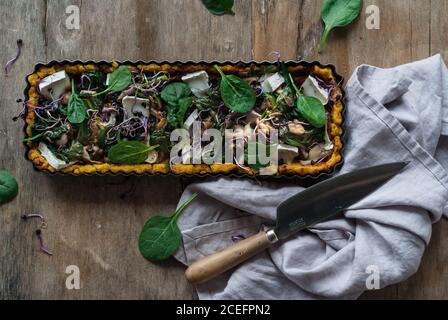 Piatto di forma metallica con crostata al forno con polenta e spinaci sormontati con pezzi di crottin su tavolo di legno Foto Stock