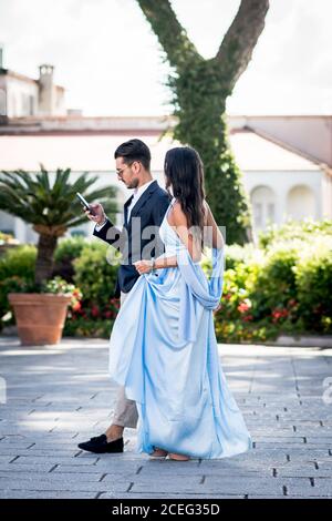 Una bella ed elegante coppia italiana si fa strada attraverso la piazza della città per partecipare a un matrimonio. Ravello, Italia. Foto Stock