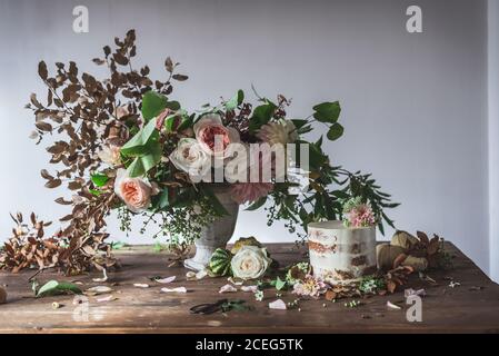 Il piatto con una gustosa torta decorata bloom bud sul tavolo di legno con mazzo di crisantemi, rose e rametti di piante in vaso tra foglie secche in backgr grigio Foto Stock