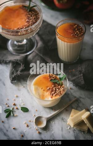 Pezzi di cioccolato bianco e cucchiaino giacenti su marmo tavolo vicino a bicchieri con deliziosa panna cotta Foto Stock