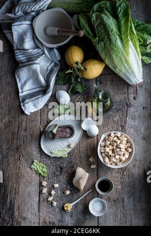 Mazzetto di vari ingredienti per piatto delizioso sdraiato su vecchio tavolo di legno vicino mortaio e pestello. Foto Stock